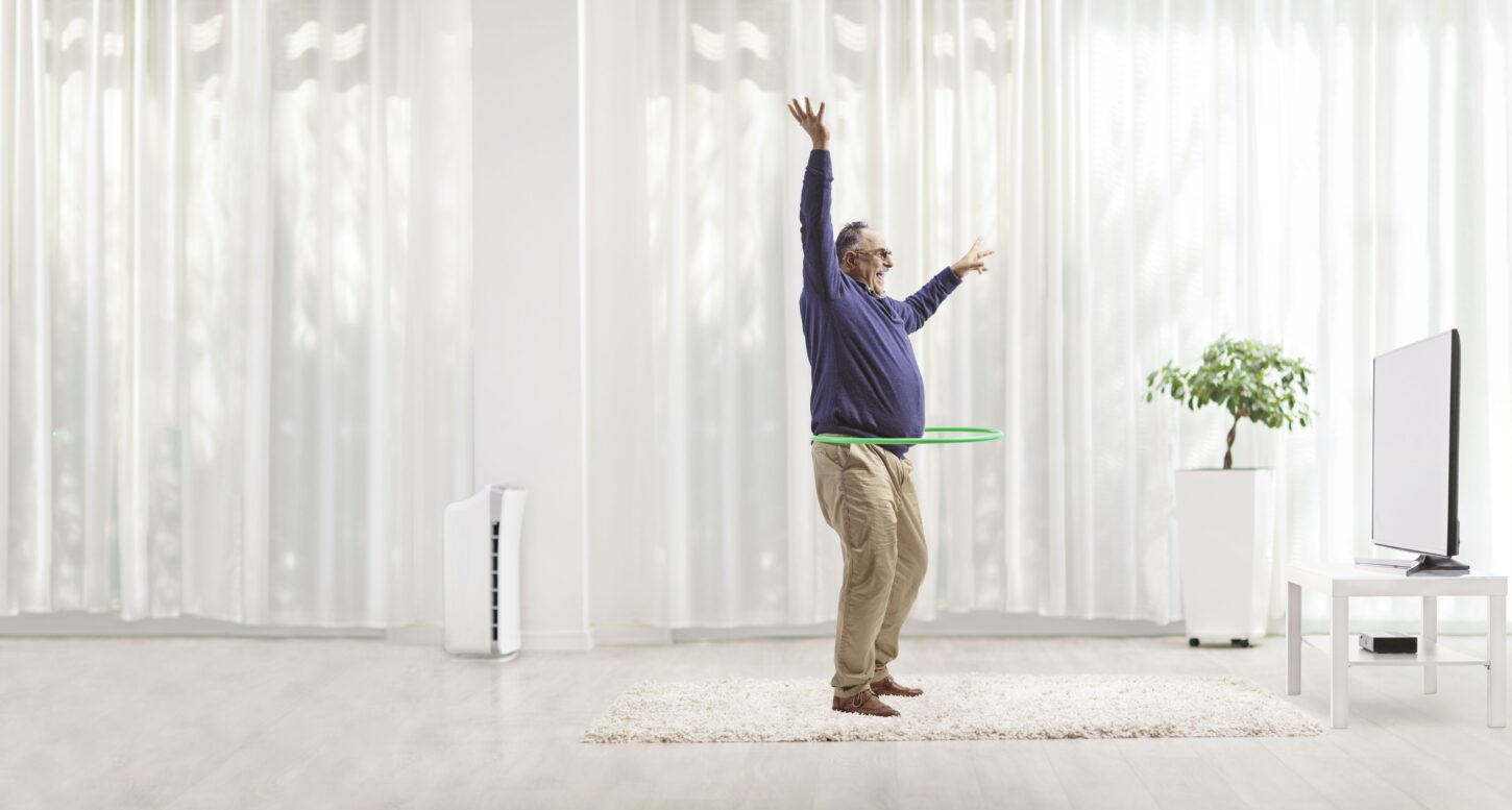 full-length-profile-shot-of-a-mature-man-spinning-a-hula-hoop-in-front-of-tv
