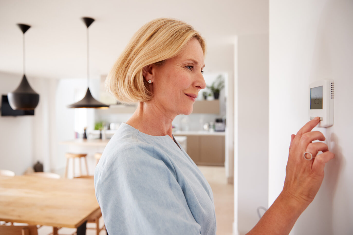 close-up-of-mature-woman-adjusting-central-heating-temperature-at-home-on-thermostat